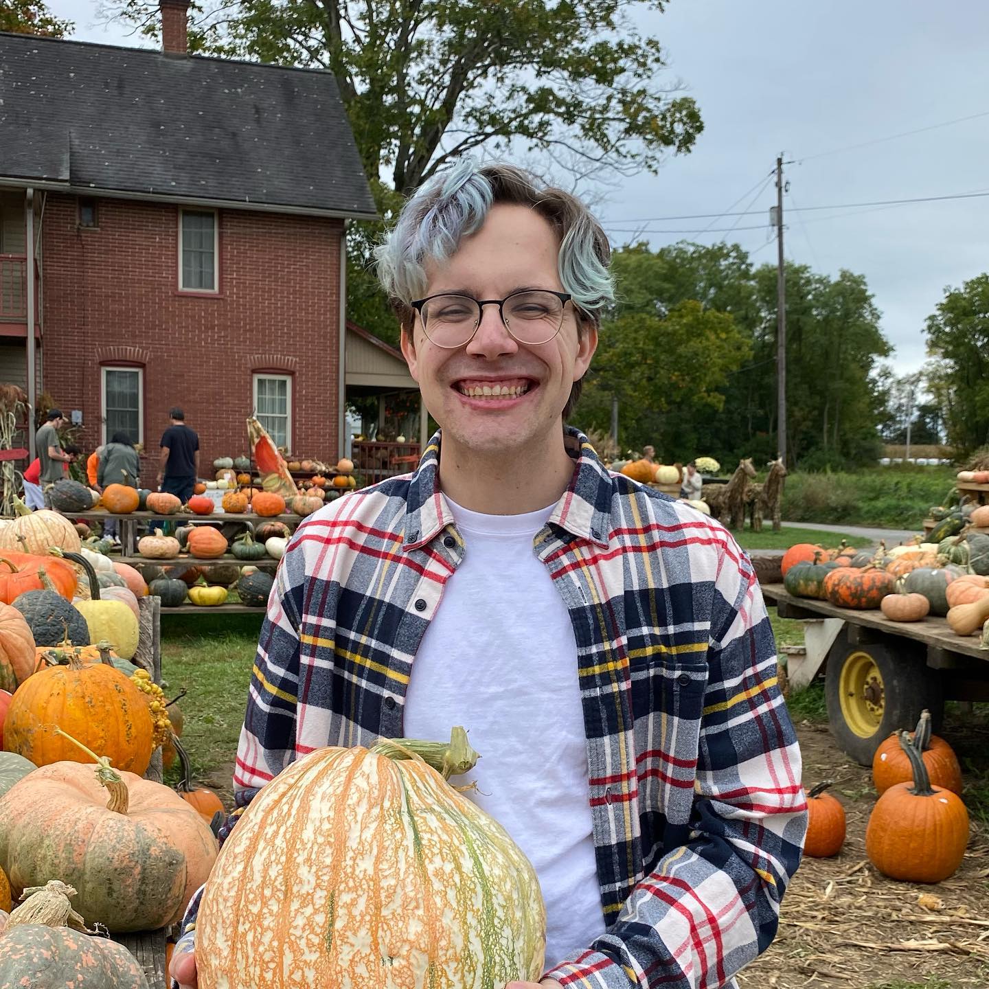 Connor smiling holding a pumpkin wearing a flannel at a farm.
